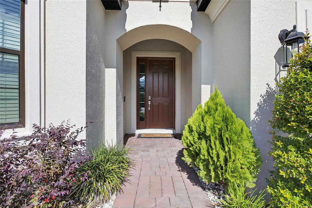 A brown front door with a side window is set within a covered arched entryway — 1910 GOBLET COVE STREET, KISSIMMEE, FL
