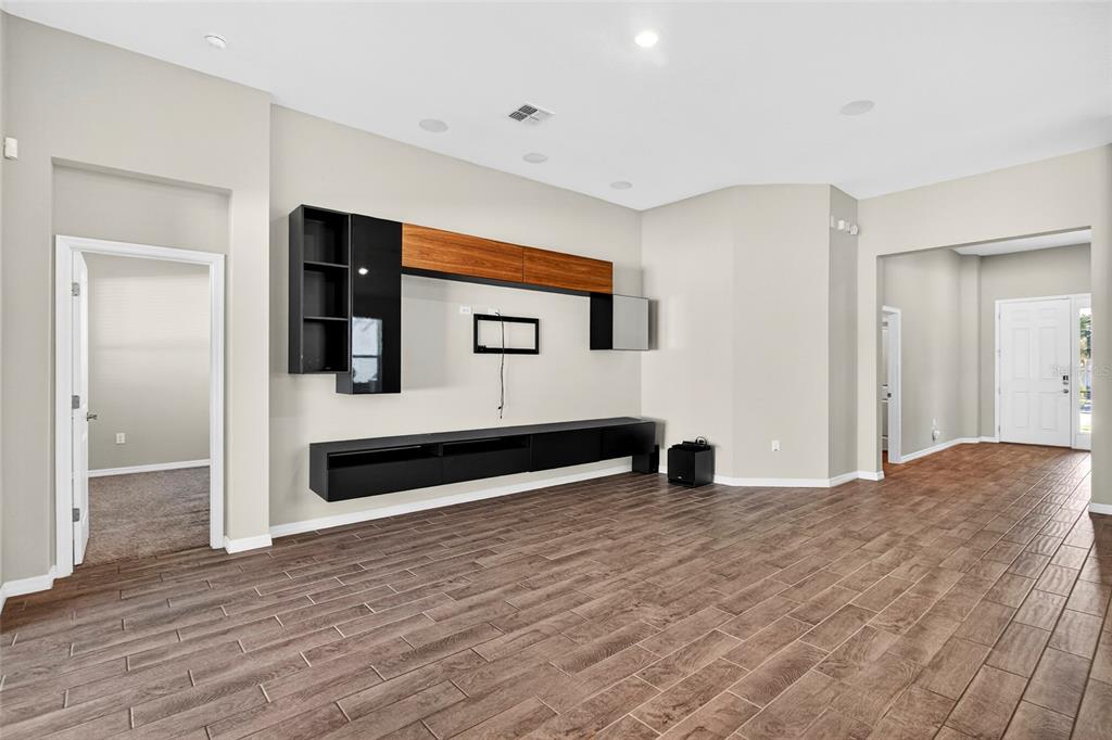 A living room features wood-look tile flooring, a wall-mounted media console, and neutral wall paint — 1910 GOBLET COVE STREET, KISSIMMEE, FL