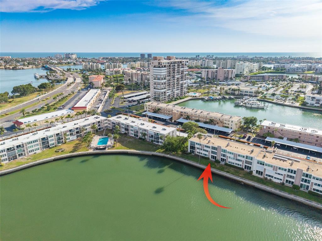 An aerial view of a waterfront condominium complex with a red arrow pointing to a unit — 7425 BAY ISLAND DRIVE S UNIT 107, ST PETERSBURG, FL