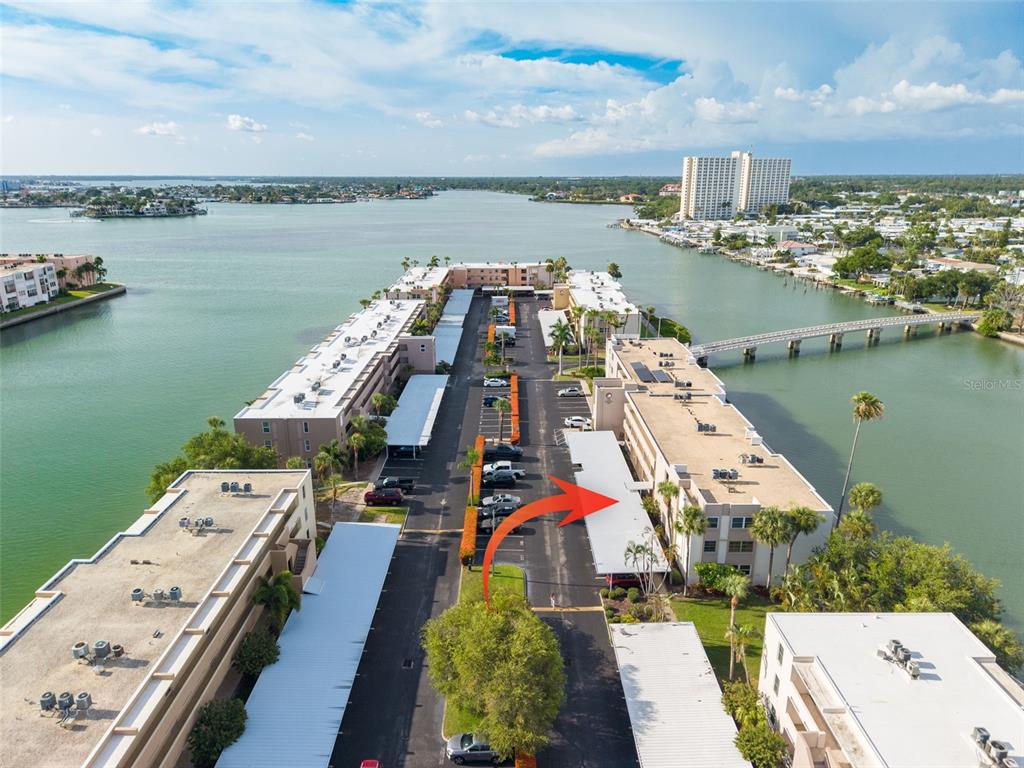 An aerial view shows multiple apartment buildings with covered parking lots situated along a waterway — 7425 BAY ISLAND DRIVE S UNIT 107, ST PETERSBURG, FL