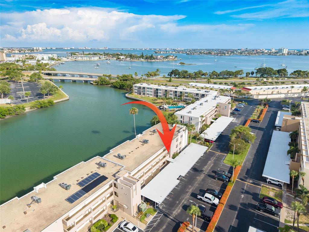 An aerial view shows a multi-story apartment building with a parking lot and waterfront access — 7425 BAY ISLAND DRIVE S UNIT 107, ST PETERSBURG, FL