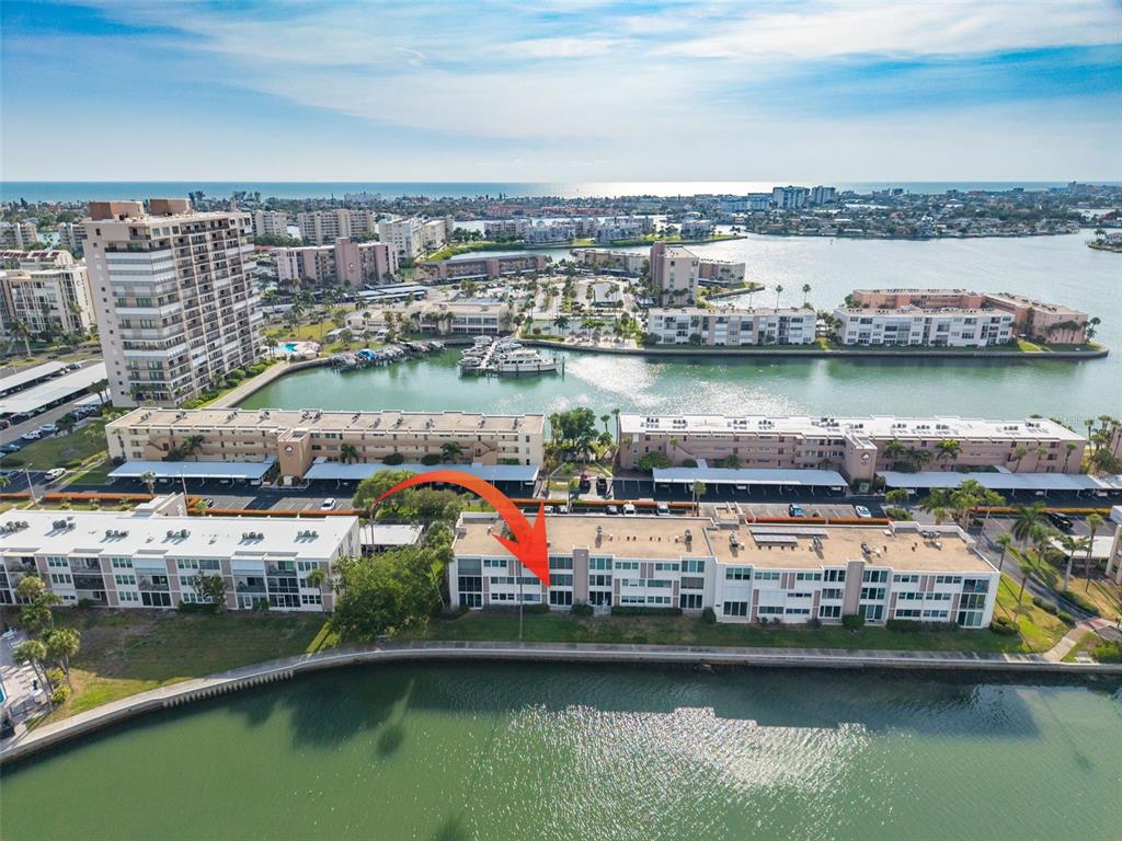 An aerial view shows a waterfront condominium complex with an orange arrow pointing to a unit — 7425 BAY ISLAND DRIVE S UNIT 107, ST PETERSBURG, FL