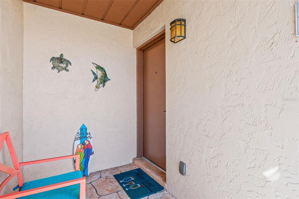 A covered entryway features a brown door, a light fixture, and coastal-themed wall decorations — 6474 DRAW LANE UNIT 77, SARASOTA, FL