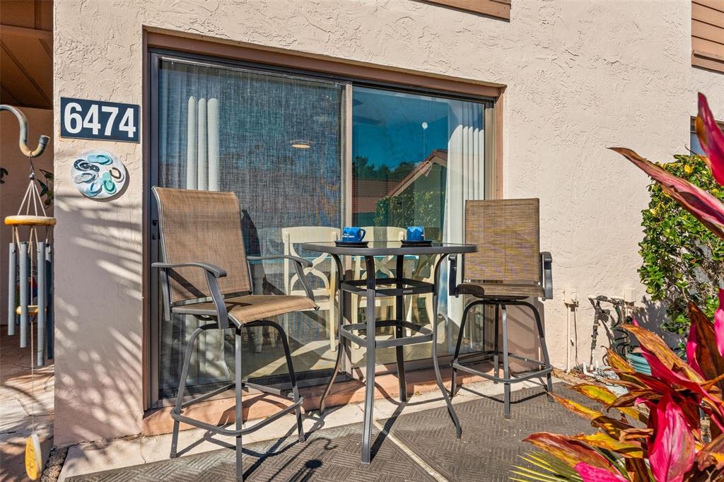 A patio features a small metal table with two chairs in front of a sliding door — 6474 DRAW LANE UNIT 77, SARASOTA, FL