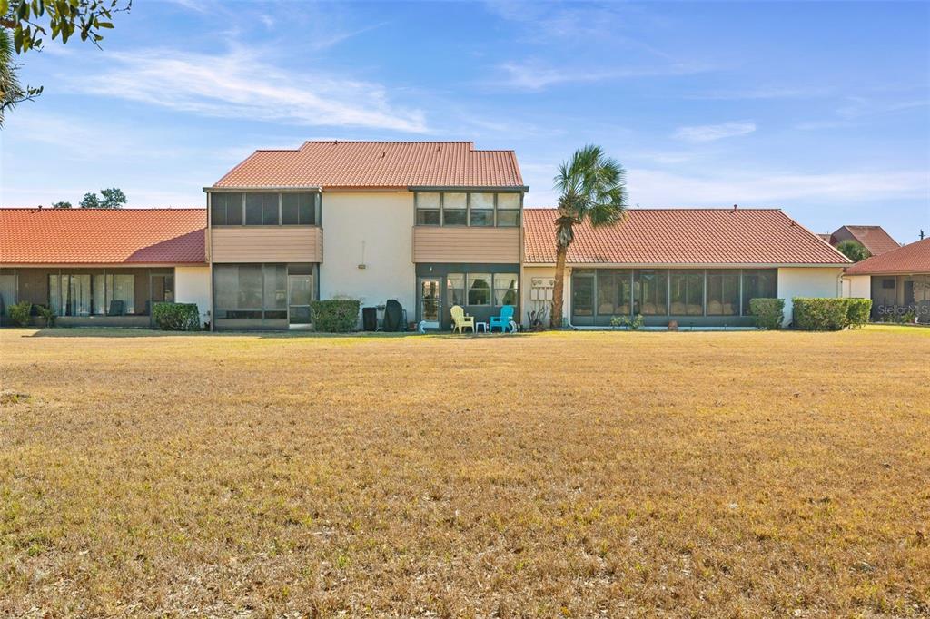 A rear view of a multi-unit residential building with a large, dry grassy lawn — 6474 DRAW LANE UNIT 77, SARASOTA, FL