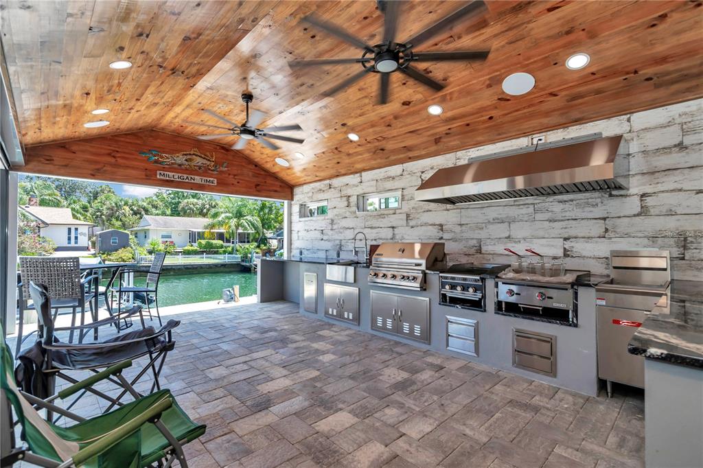 An outdoor kitchen with stainless steel appliances, wood-paneled ceiling, and stone flooring overlooks a canal — 1409 SE 4TH AVENUE, CRYSTAL RIVER, FL