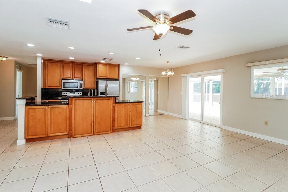 A kitchen with wood cabinets and tile flooring opens into a spacious living area — 1701 E ORANGESIDE ROAD, PALM HARBOR, FL