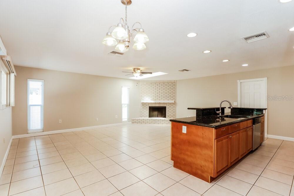An open-concept kitchen and living area with tile floors, a brick fireplace, and island seating — 1701 E ORANGESIDE ROAD, PALM HARBOR, FL