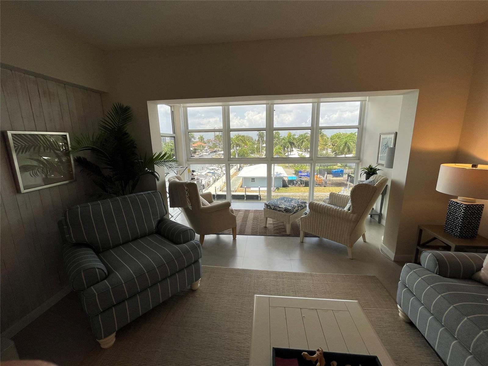 A living room features striped armchairs, a windowed alcove with water views, and tile flooring — 1481 S Ocean Boulevard # A, Pompano Beach FL 33062, POMPANO BEACH, FL