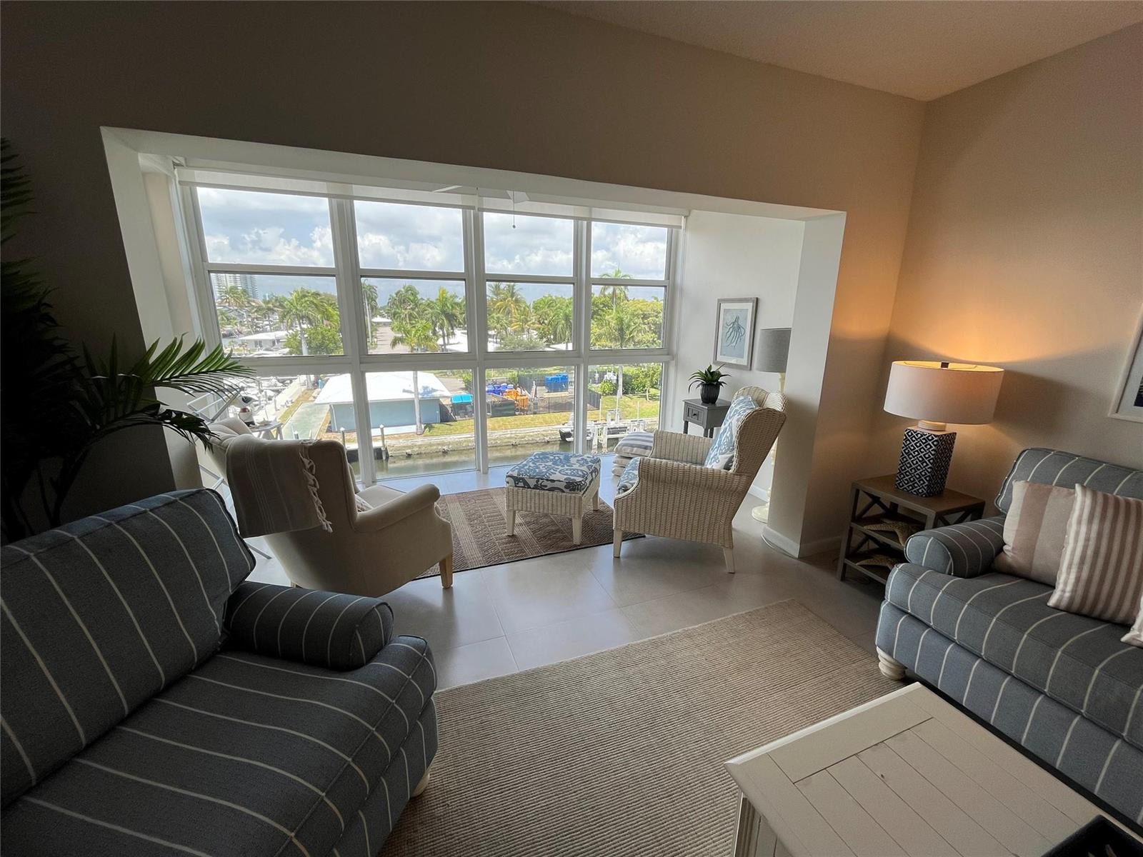 A living room with striped sofas, wicker chairs, and a large window overlooking a canal — 1481 S Ocean Boulevard # A, Pompano Beach FL 33062, POMPANO BEACH, FL