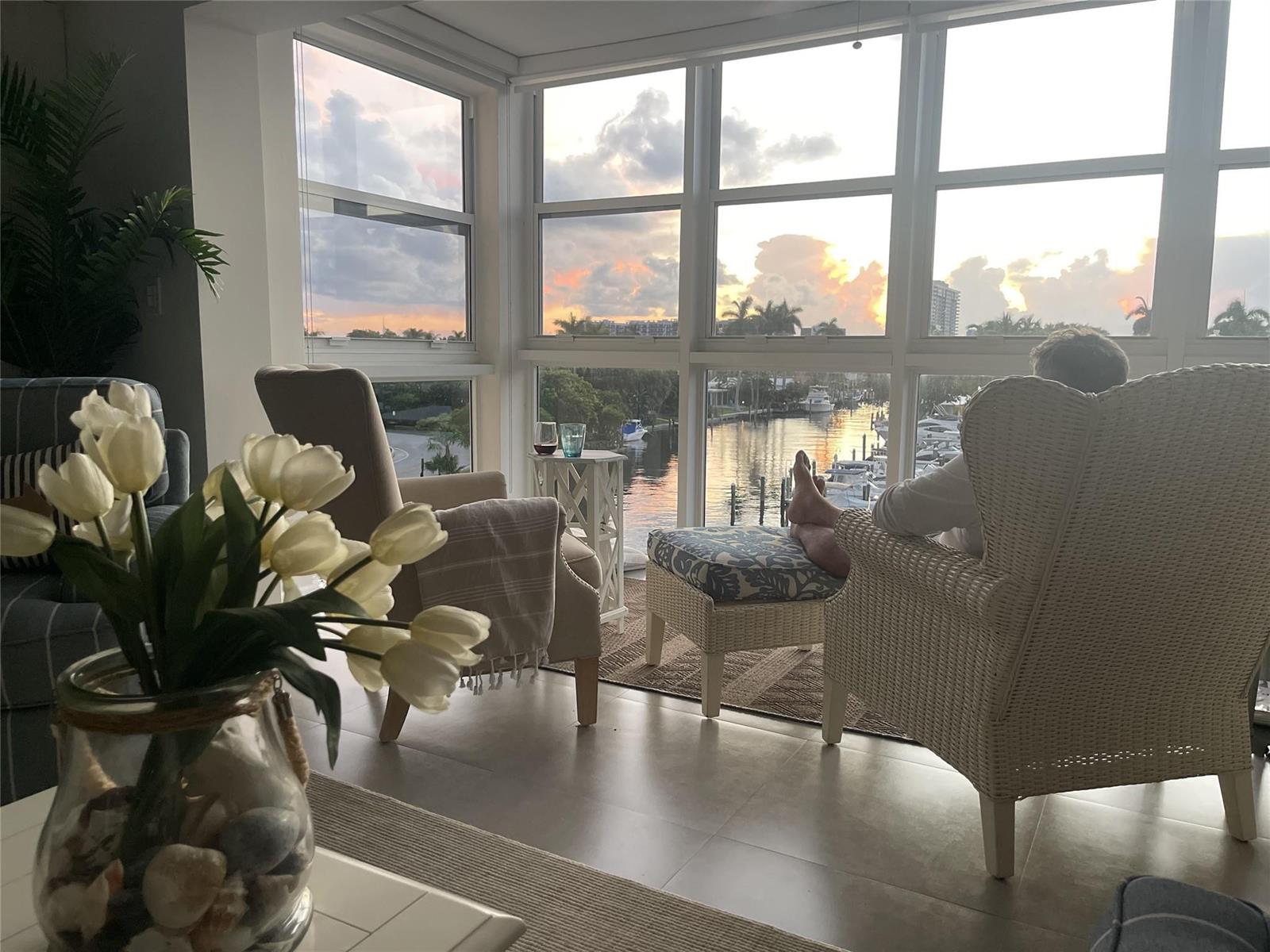 A living room with floor-to-ceiling windows overlooking a canal with boats at sunset — 1481 S Ocean Boulevard # A, Pompano Beach FL 33062, POMPANO BEACH, FL