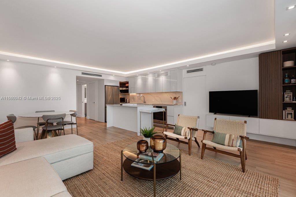 A modern open-concept living room and kitchen feature light wood floors and white cabinetry — 2301 Collins Ave # 837, Miami Beach FL 33139, MIAMI BEACH, FL