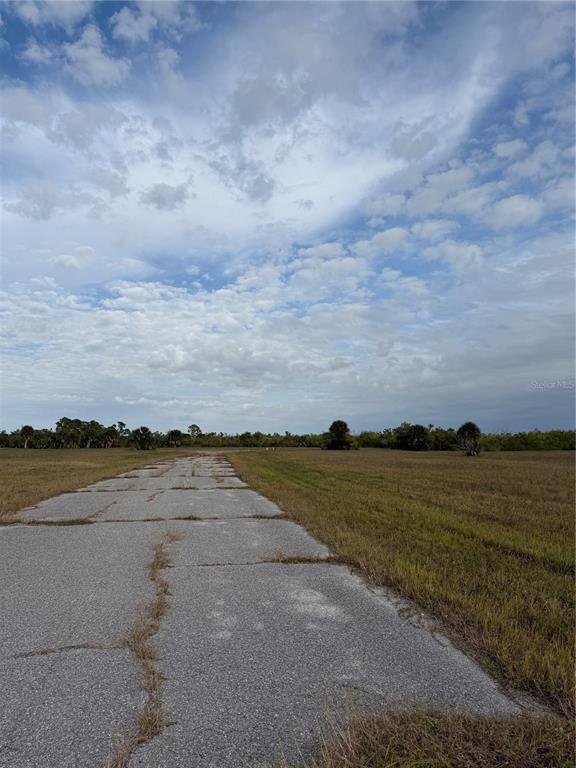 A cracked concrete path leads through a flat, grassy field under a cloudy sky — 14495 MARLIN COURT, PLACIDA, FL