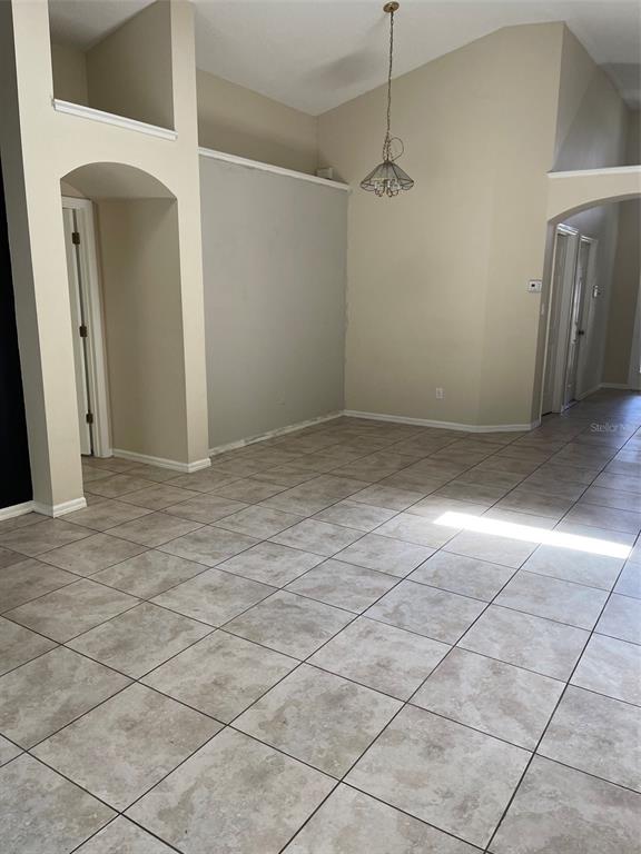 An empty room with beige tile flooring, vaulted ceilings, and an arched doorway — 1908 BOBTAIL DR, MAITLAND, FL