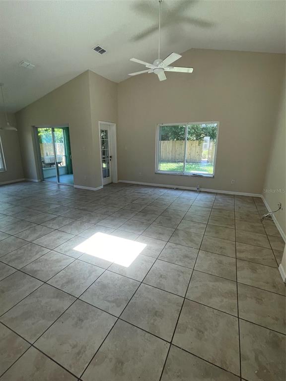 A spacious living room features vaulted ceilings, tile flooring, a ceiling fan, and large windows — 1908 BOBTAIL DR, MAITLAND, FL