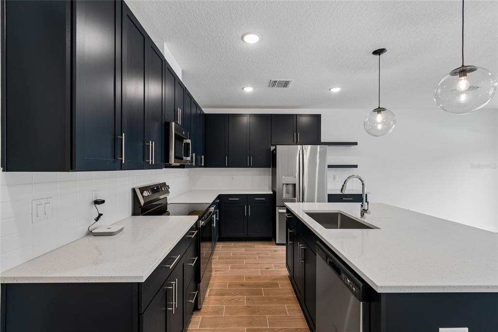 A modern kitchen features dark cabinets, white countertops, stainless steel appliances, and wood-look tile flooring — 3406 WITHERS WAY, DAVENPORT, FL