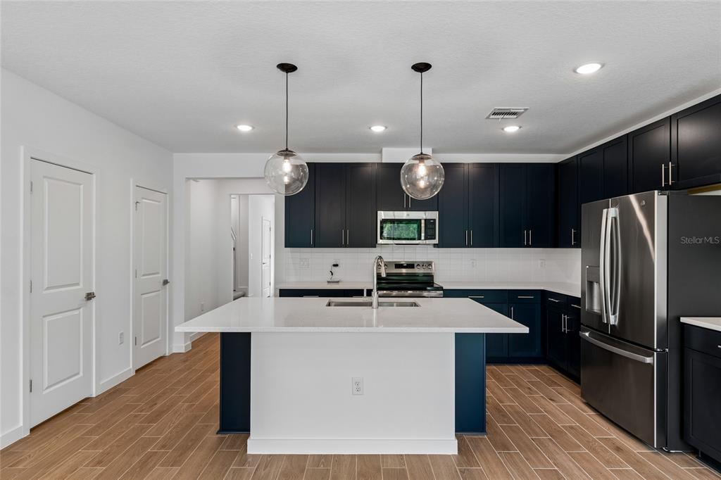 A kitchen features dark blue cabinetry, a white quartz island, and stainless steel appliances — 3406 WITHERS WAY, DAVENPORT, FL
