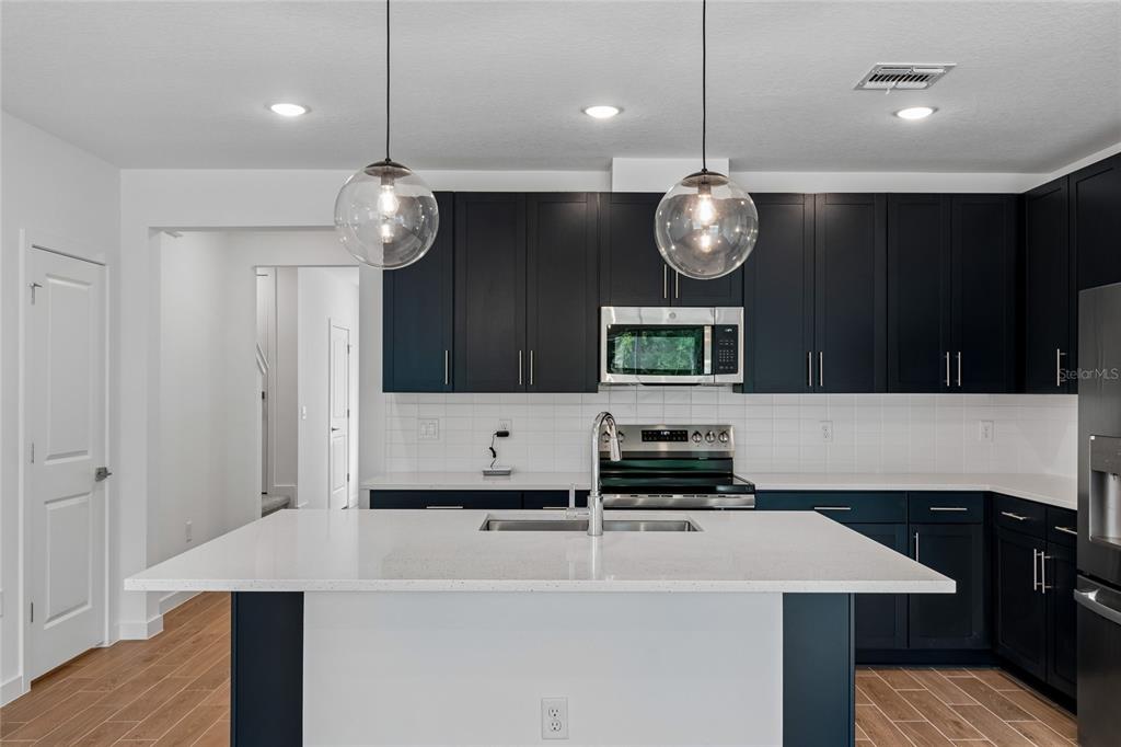 A modern kitchen features dark cabinets, white countertops, a central island, and two pendant lights — 3406 WITHERS WAY, DAVENPORT, FL