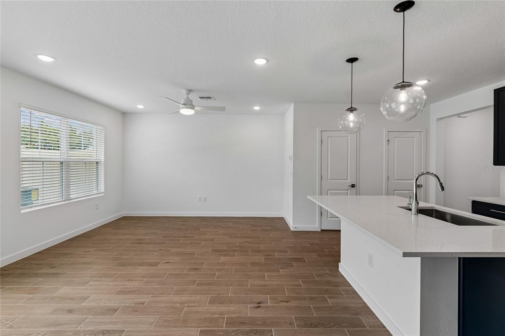 An open-concept room features wood-look tile flooring, a kitchen island with a sink, and pendant lighting — 3406 WITHERS WAY, DAVENPORT, FL