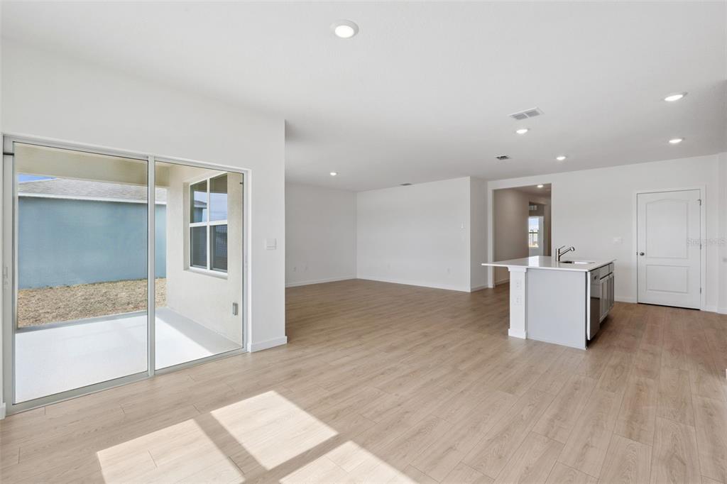 An open-concept living area with light wood-look flooring, a kitchen island, and sliding glass doors — 4922 MARSHELDER STREET, APOPKA, FL