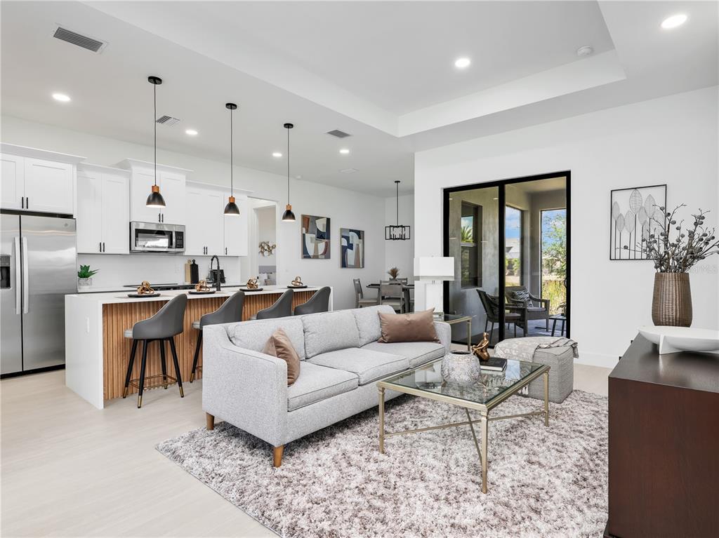An open-concept kitchen and living area features white cabinetry, a wood-slatted island, and sliding glass doors — 1704 NW 6TH PLACE, CAPE CORAL, FL