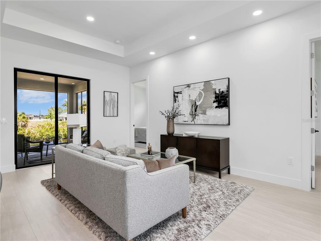 A modern living room features a grey sofa, a dark console table, and sliding glass doors — 1704 NW 6TH PLACE, CAPE CORAL, FL