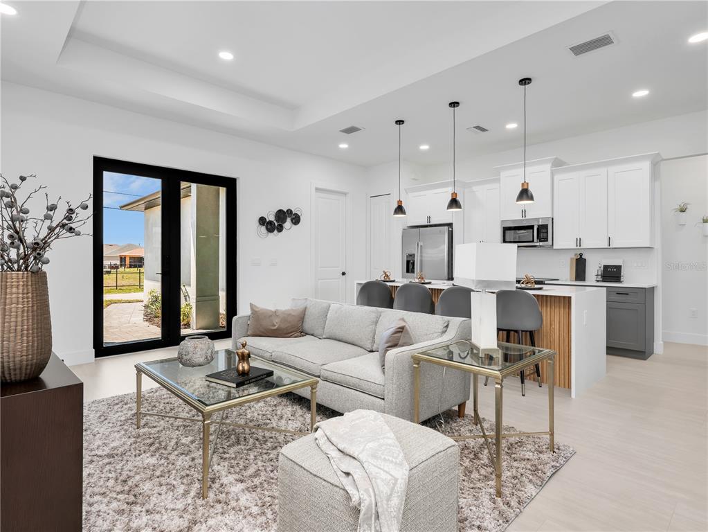 A modern open-concept living room and kitchen featuring white cabinetry, gray seating, and glass tables — 1704 NW 6TH PLACE, CAPE CORAL, FL