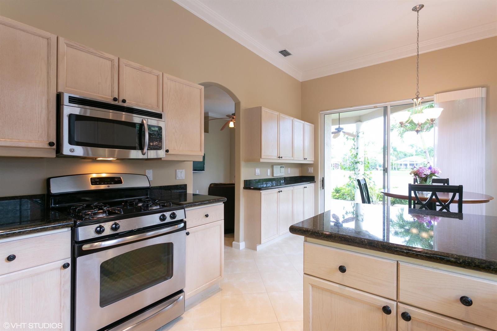 A kitchen features light wood cabinets, dark granite countertops, stainless steel appliances, and a dining area — 8407 Quail Meadow Way, West Palm Beach FL 33412, WEST PALM BEACH, FL