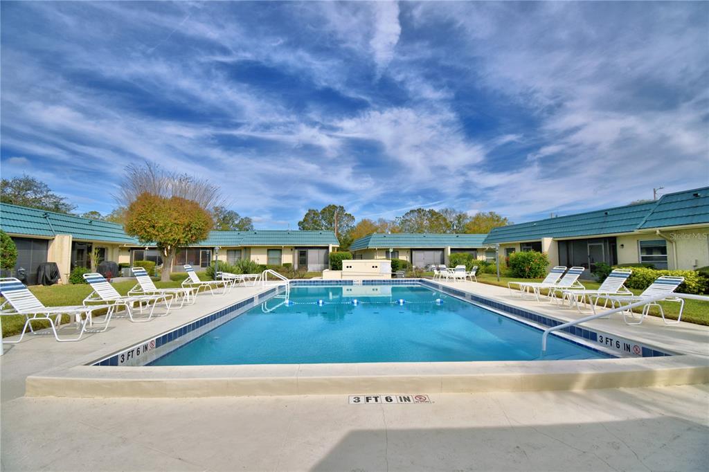 An outdoor swimming pool is surrounded by lounge chairs and single-story residential buildings — 345 24TH STREET NW UNIT 25, WINTER HAVEN, FL
