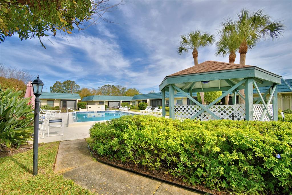A swimming pool sits beside a wooden gazebo in a residential courtyard with palm trees — 345 24TH STREET NW UNIT 25, WINTER HAVEN, FL