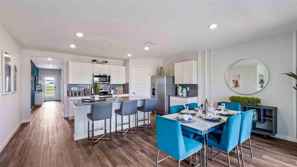 A modern open-concept kitchen and dining area with white cabinetry, blue chairs, and wood flooring — 18312 BEEHIVE TERRACE, LAKEWOOD RANCH, FL