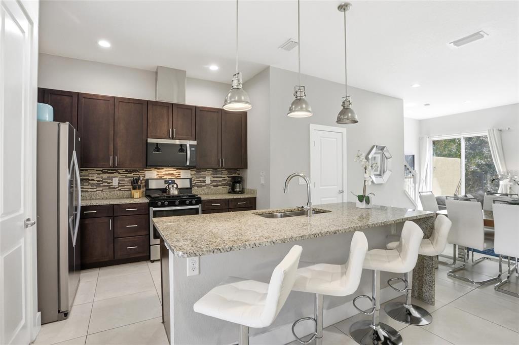 A modern kitchen features dark wood cabinets, granite countertops, an island, and three bar stools — 7540 SUNVILLE AVENUE, KISSIMMEE, FL