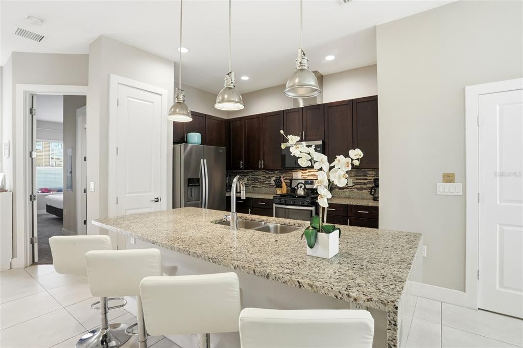 A kitchen features dark wood cabinets, granite countertops, a central island, and white bar stools — 7540 SUNVILLE AVENUE, KISSIMMEE, FL