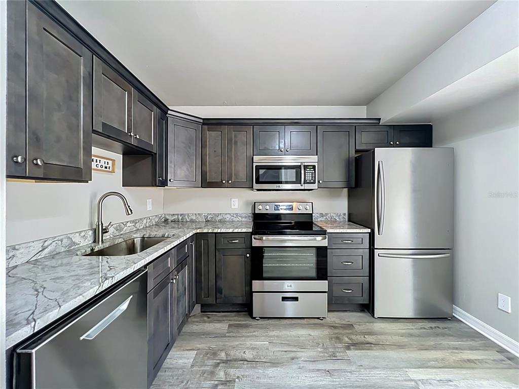 A kitchen features dark wood cabinets, stainless steel appliances, and gray marble-patterned countertops — 2312 S PARK AVENUE, SANFORD, FL