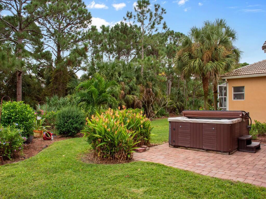 A brown hot tub sits on a brick patio in a backyard with lush landscaping — 6159 Arlington Way, Fort Pierce FL 34951, FORT PIERCE, FL