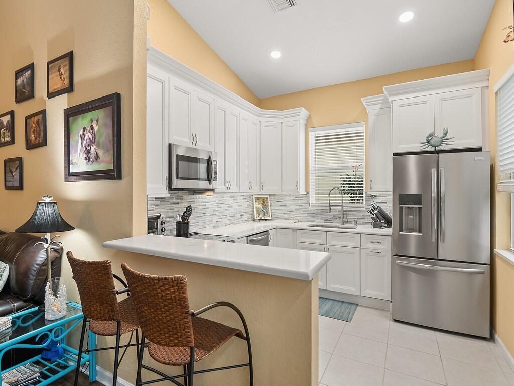 A kitchen features white cabinets, stainless steel appliances, a breakfast bar, and light-colored tile flooring — 6159 Arlington Way, Fort Pierce FL 34951, FORT PIERCE, FL
