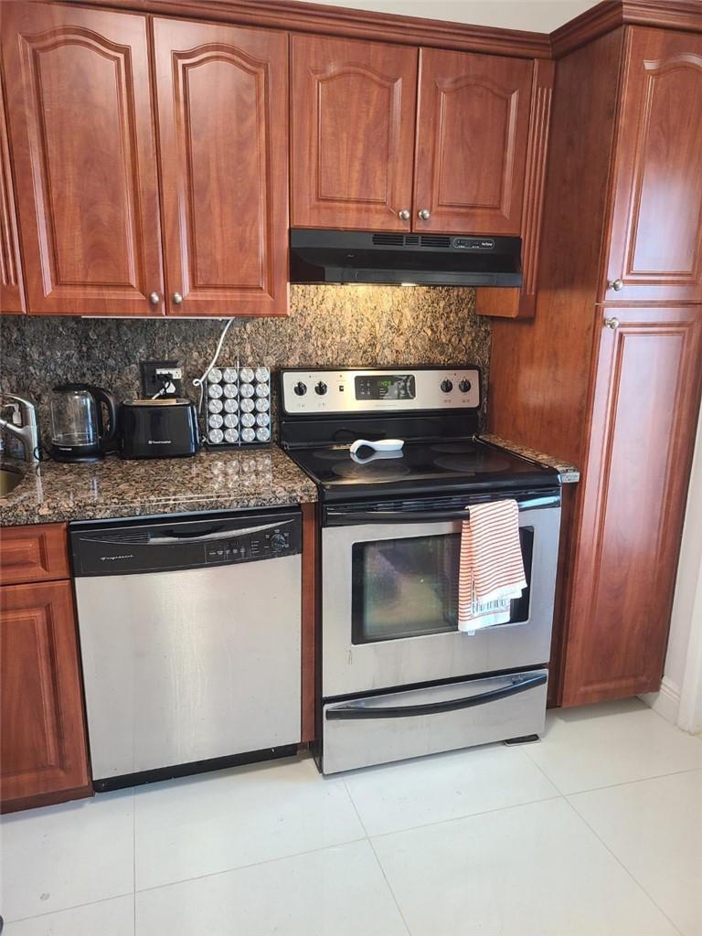 A kitchen features wood cabinets, granite countertops, and stainless steel appliances — 3091 N Course Drive # 208, Pompano Beach FL 33069, POMPANO BEACH, FL