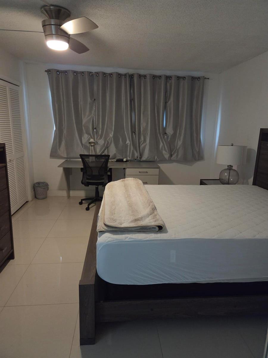 A bedroom features a bed, a desk with a chair, and gray curtains over a window — 3091 N Course Drive # 208, Pompano Beach FL 33069, POMPANO BEACH, FL