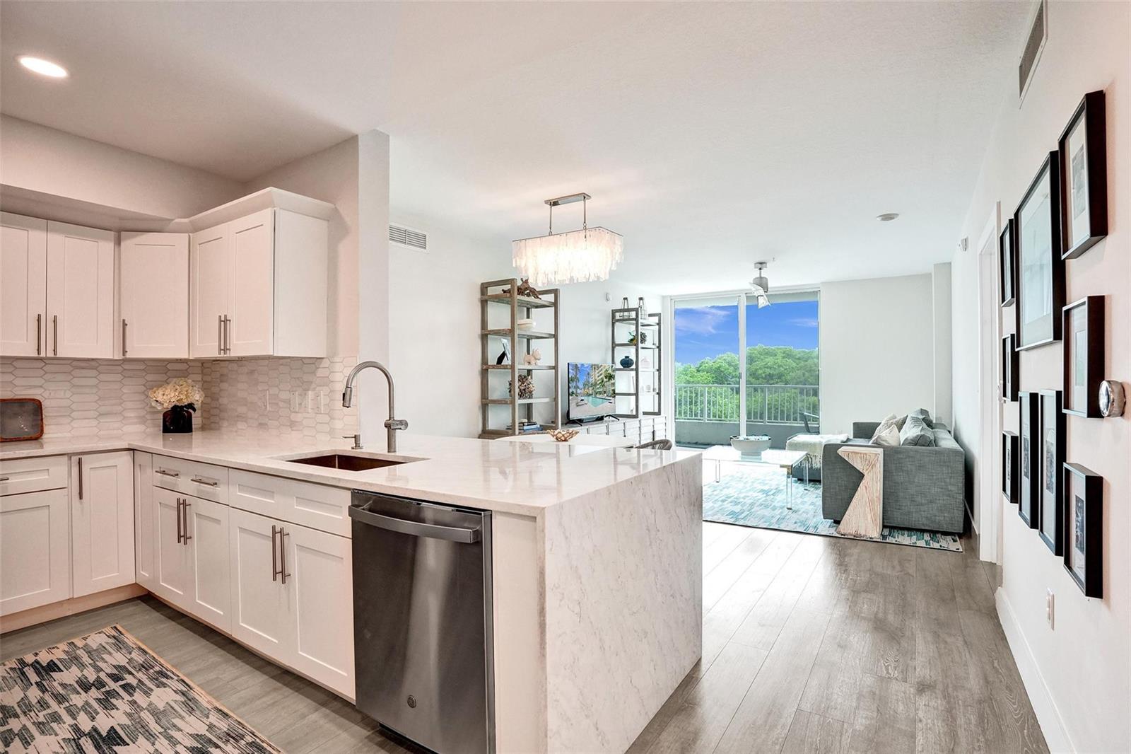 A modern kitchen with white cabinets and marble countertops opens into a living room area — 700 E Boynton Beach Boulevard # 406, Boynton Beach FL 33435, BOYNTON BEACH, FL
