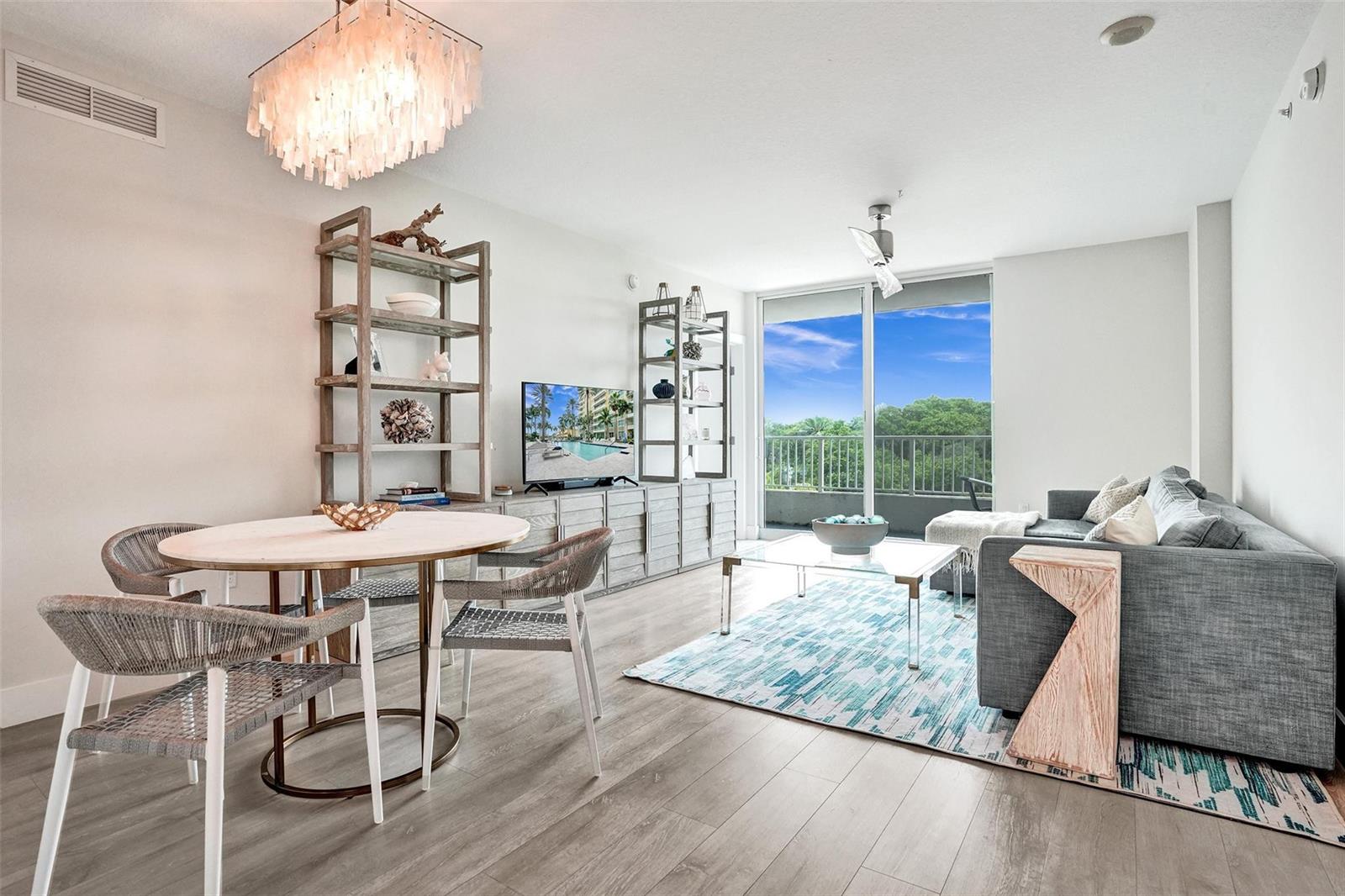 A bright living and dining area features light wood floors, a chandelier, and balcony access — 700 E Boynton Beach Boulevard # 406, Boynton Beach FL 33435, BOYNTON BEACH, FL