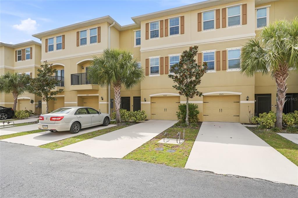 A row of three-story townhomes with beige stucco exteriors, tan garage doors, and palm trees — 5523 YELLOWFIN COURT, NEW PORT RICHEY, FL
