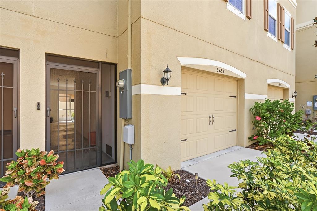 The exterior of a tan townhouse features a front door with a screen and garage — 5523 YELLOWFIN COURT, NEW PORT RICHEY, FL
