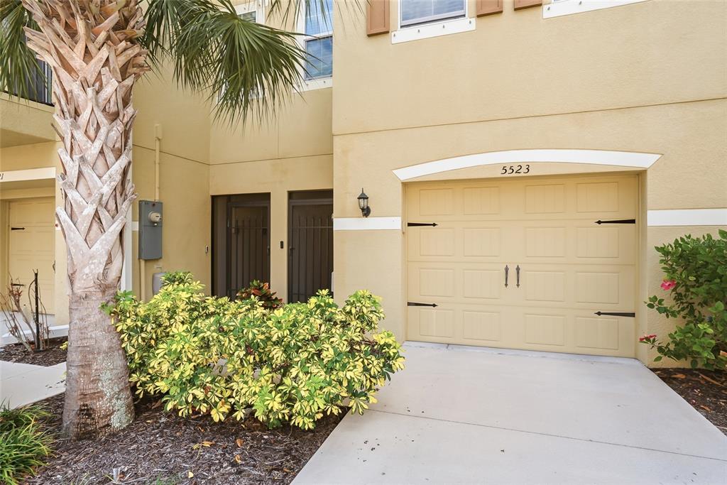 A beige townhouse exterior features a single-car garage, a palm tree, and landscaping — 5523 YELLOWFIN COURT, NEW PORT RICHEY, FL