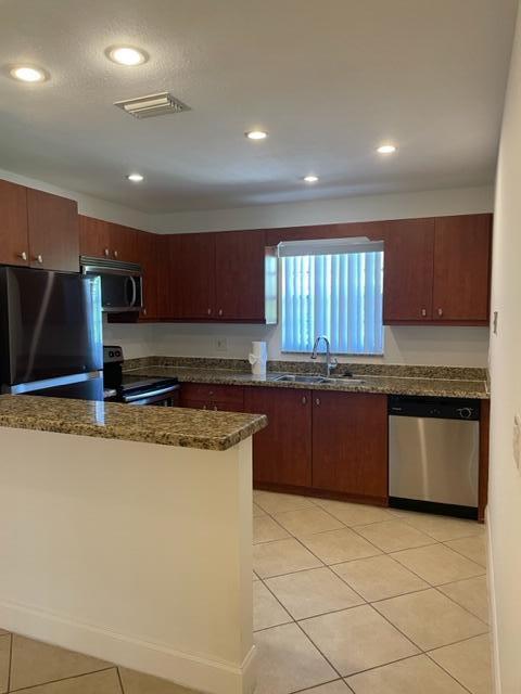 A kitchen features wood cabinets, granite countertops, stainless steel appliances, and light tile flooring — 1971 Juno Road, North Palm Beach FL 33408, NORTH PALM BEACH, FL