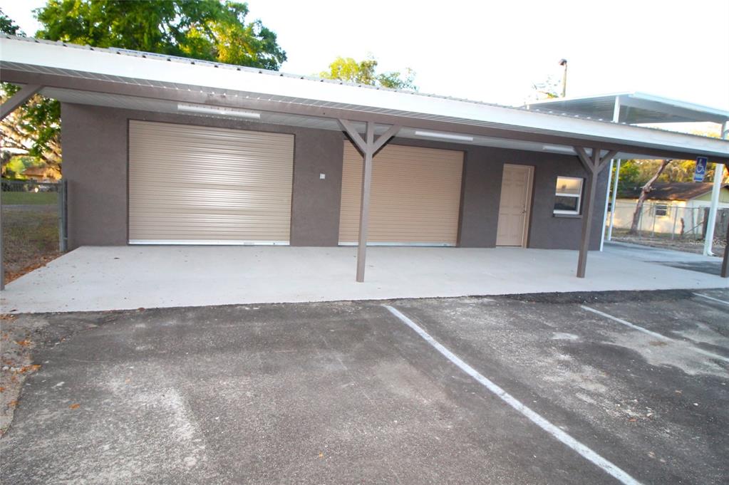 A brown building features two roll-up garage doors, a single door, and a covered patio — 114 W MYERS BOULEVARD, MASCOTTE, FL