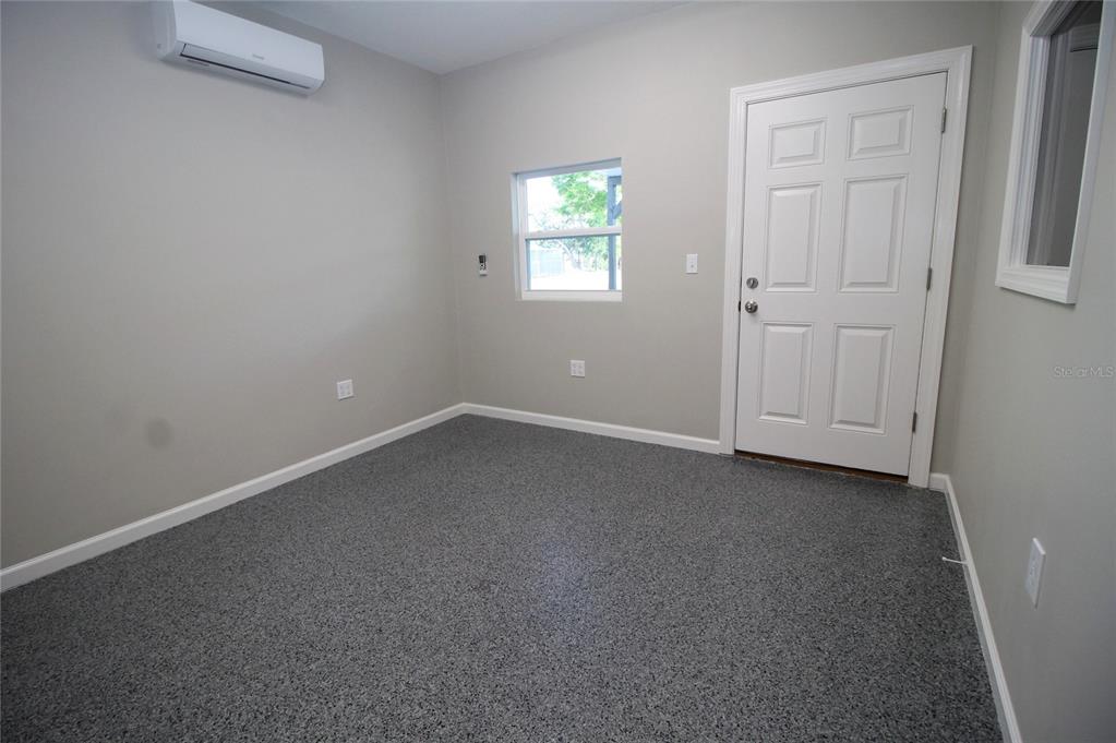 A small room features gray walls, a speckled epoxy floor, a window, and a wall-mounted AC — 114 W MYERS BOULEVARD, MASCOTTE, FL
