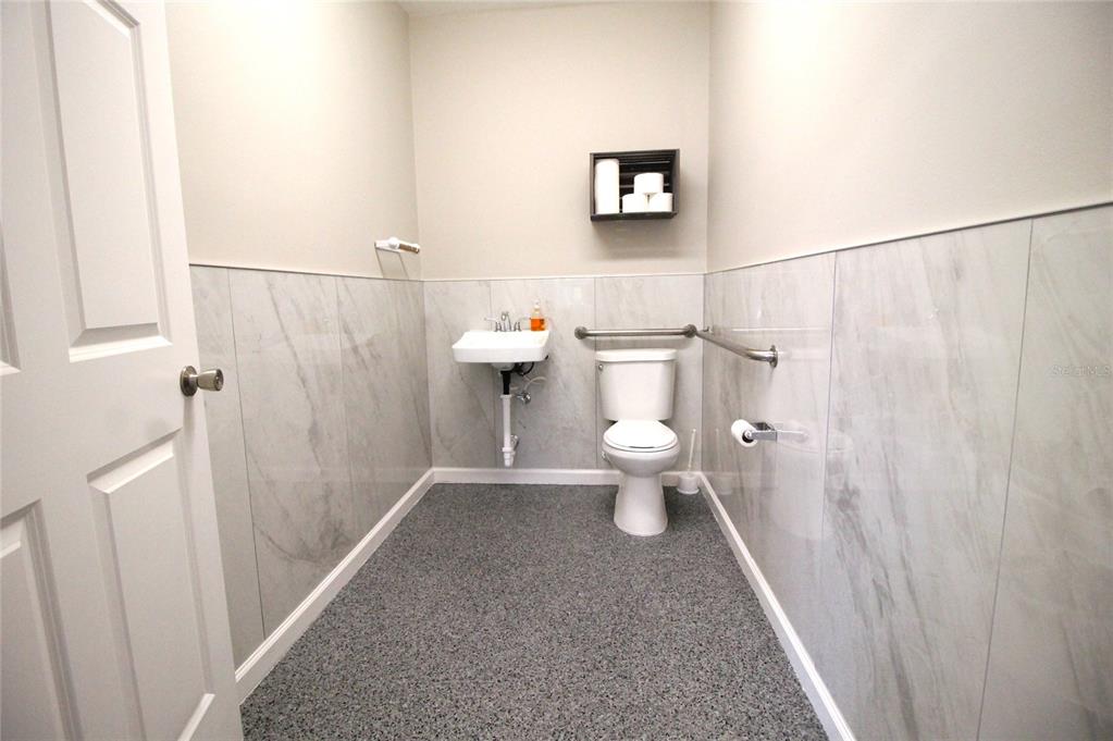 A small bathroom features a wall-mounted sink, a toilet with grab bars, and marble-look tiling — 114 W MYERS BOULEVARD, MASCOTTE, FL