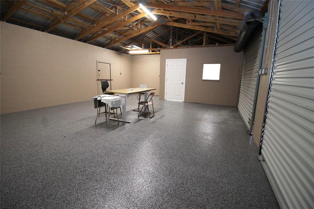 An interior view of a garage with a speckled epoxy floor and exposed wooden rafters — 114 W MYERS BOULEVARD, MASCOTTE, FL