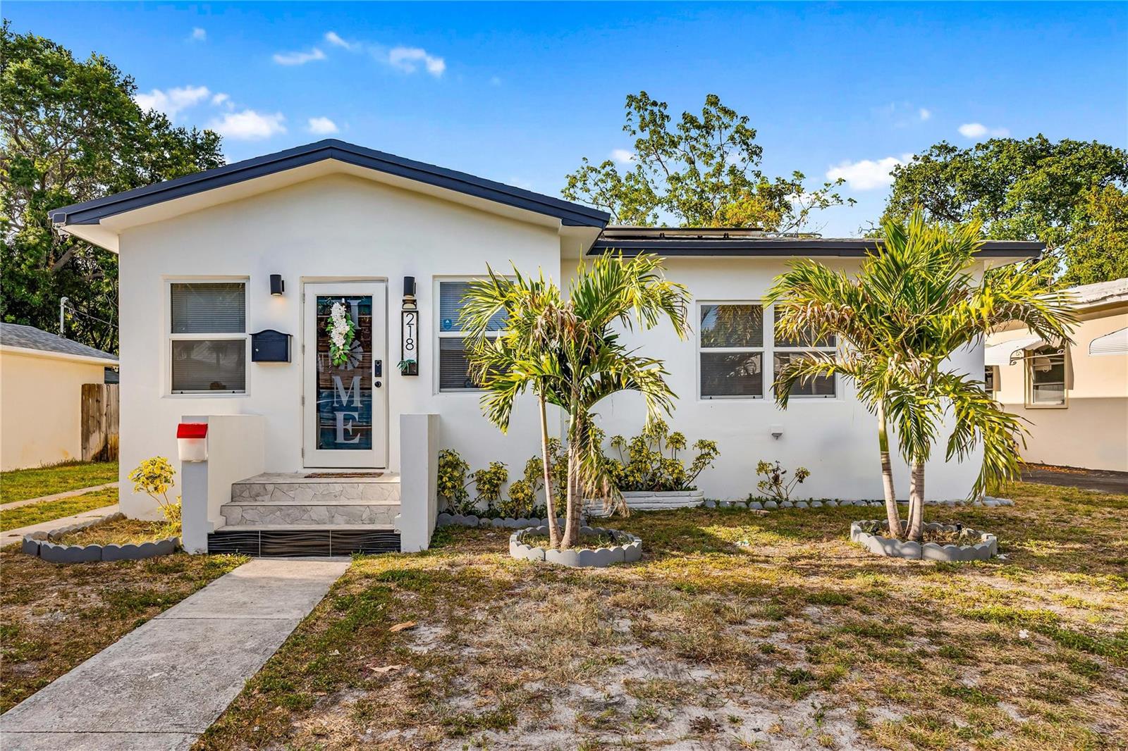 A white single-story house features a front door, two palm trees, and a concrete walkway — 218 SW 7th Street, Dania Beach FL 33004, DANIA BEACH, FL
