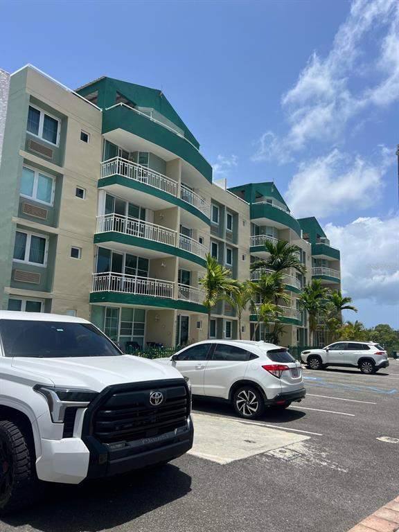 A multi-story apartment building with green accents and balconies stands behind a parking lot — VISTA DEL MAR LUXURY BARRIO ARENALES ROAD 110 UNIT C 201, AGUADILLA, PR